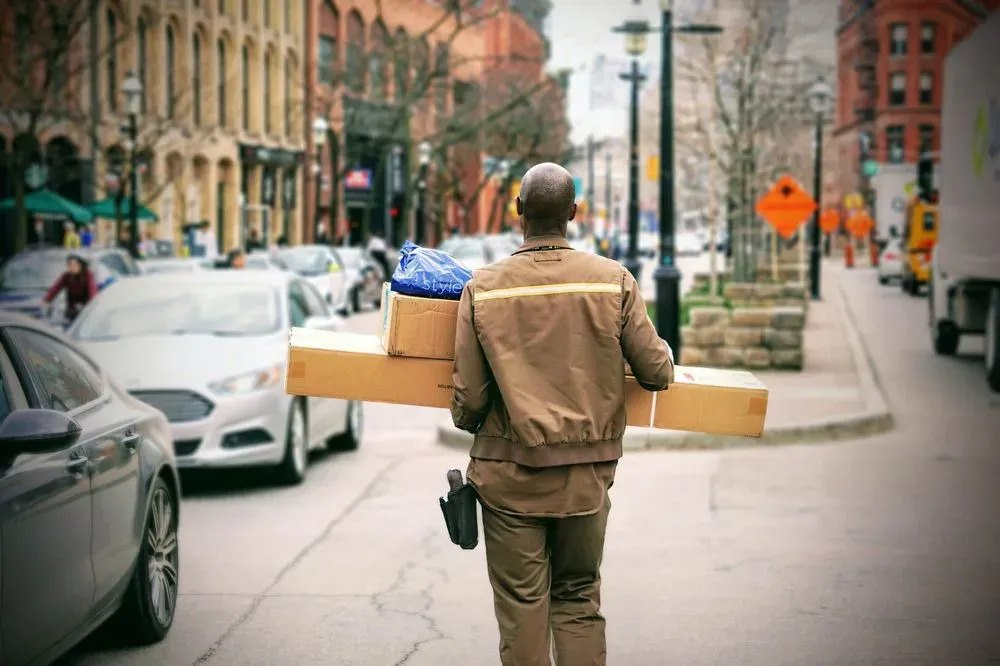 A courier walking down a city street, carrying multiple packages