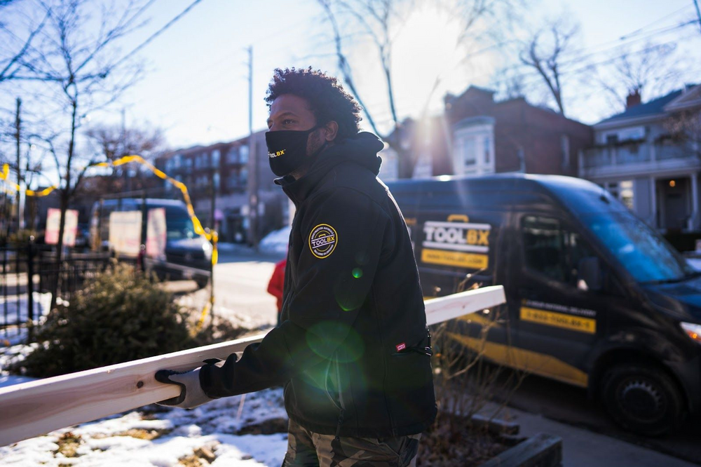 Worker carrying wooden beam next to TOOLBX van on a snowy street